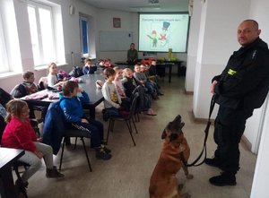 Uczestnicy spotkania podczas zajęć. Policjant z psem policyjnym na pierwszym planie.