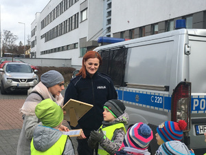 Dzieci wraz z opiekunami i policjantką przy policyjnym radiowozie.