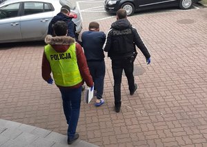 trzej policjanci prowadzą zatrzymanego skutego kajdankami zespolonymi