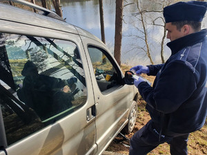 Policjant podczas czynności przy aucie zaparkowanym przy nabrzeżu Zalewu Koronowskiego.