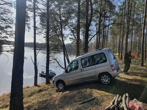 Auto, którym mężczyźni przyjechali na piknik do lasu. w tle policyjna łódź motorowa na wodzie oraz funkcjonariusz Państwowej Straży Rybackiej stojący przy aucie.