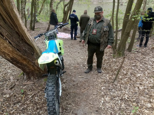 Leśnik stoi przy motocyklu. W tle policjant rozmawiający z mężczyznami.