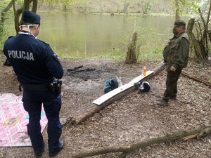 Policjant i leśnik stoją przy zagaszonym ognisku w lesie.