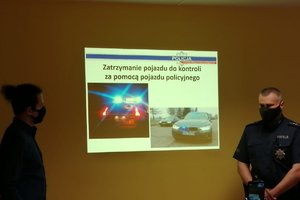 policjant omawia wyświetlane slajdy. Po przeciwnej stronie stoi tłumacz