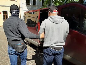 Policjant wyprowadza zatrzymanego z auta przed prokuraturą.