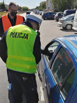 Policjant wręcza nagrodzonemu kierowcy upominek. W tle przedstawiciel Bydgoskiego Zarządu Dróg Miejskich i Komunikacji Publicznej.