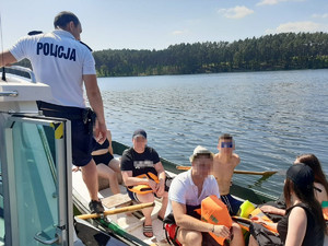 Policjant podczas kontroli łódki z kilkoma osobami.