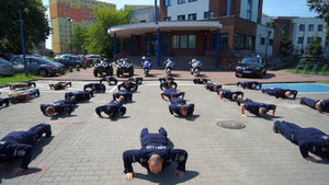 policjanci robią pompki na parkingu przed komendą miejską