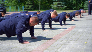 policjanci robią pompki na parkingu przed komendą miejską