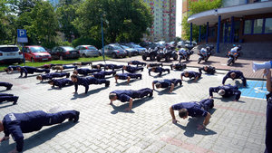 policjanci robią pompki na parkingu przed komendą miejską