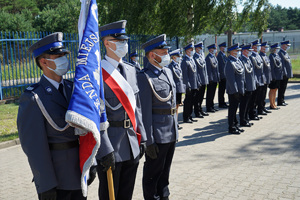 poczet sztandarowy. W oddali stoją policjanci w szeregu