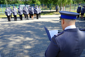 Komendant czyta list. W oddali stoją policjanci w szeregu