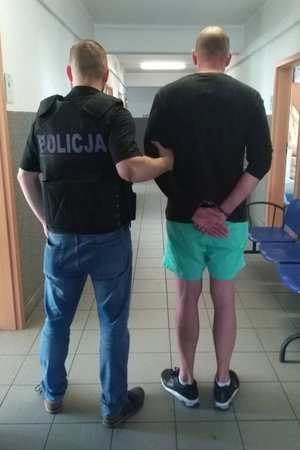 policjant trzyma zatrzymanego skutego kajdankami