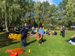 Policjanci rozmawiając z uczniami prezentują sprzęt do udzielania pomocy na wodzie.