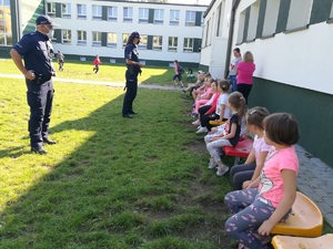 Policjanci rozmawiają z uczniami siedzącymi na ławkach na terenie przyszkolnym.