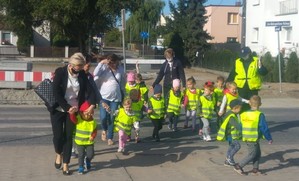 Dzieci wraz z opiekunkami przechodzą przejście dla pieszych w budowie. Wszystko pod okiem policjantki, która idzie z nimi.