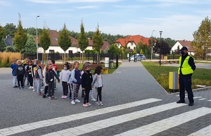 Policjant z dziećmi stoją przed przejściem dla pieszych.