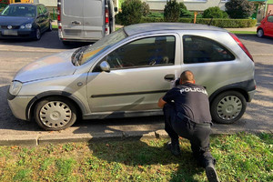 policjant klęczy przed przednimi drzwiami opla od strony kierowcy i fotografuje zamek drzwi