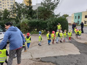 dzieci w kamizelkach odblaskowych idą chodnikiem w stronę przejścia dla pieszych.