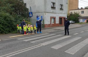 dzieci wraz z polfinkiem oczekują na przejście po pasach przez ulicę.