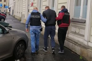 dwaj policjanci ubrani po cywilnemu prowadzą zatrzymanego skutego kajdankami zespolonymi założonymi na ręce z przodu oraz na nogi