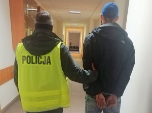 policjant prowadzi zatrzymanego skutego kajdankami założonymi na ręce trzymane z tyłu