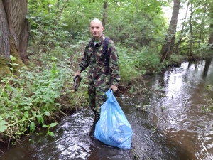 Marcin Sikora stoi w strumyku i trzyma w ręce śmieci oraz worek ze śmieciami