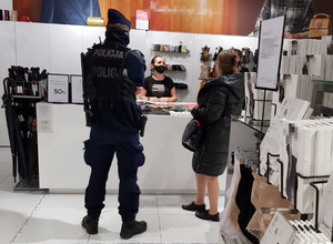 Pracownik Sanepidu wraz z policjantem rozmawiają z pracownicą sklepu stojącą za ladą.