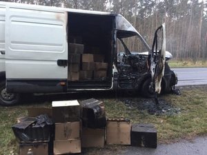 Auto dostawcze częściowo spalone. W przestrzeni załadunkowej widoczne przez otwarte drzwi kartony. Kilka kartonów stoi również na poboczu przez autem.