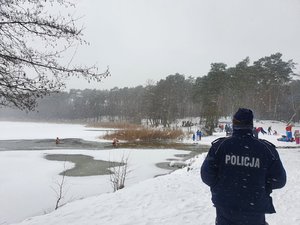 Policjant stoi przy zamarzniętym jeziorze.