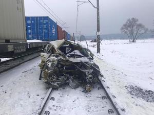 uszkodzony biały peugeot stoi na torach, a obok stoją wagony