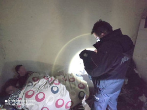 Patrol rozmawia z bezdomnymi, którzy leżą w łóżku przykryci kołdrą.