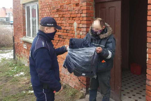 Policjant przekazuje bezdomnemu kurtko-śpiwór.