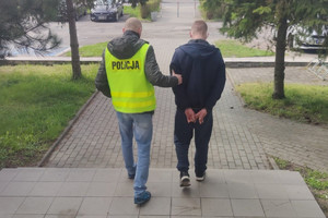 policjant prowadzi zatrzymanego skutego kajdankami