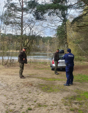 Policjant i dwaj leśnicy przy aucie, które zaparkowało na nabrzeżu mimo zakazu.