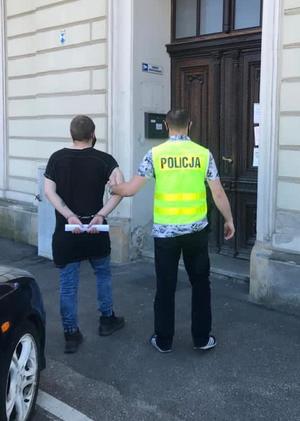 Policjant prowadzi zatrzymanego do budynku prokuratury.