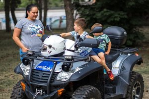 Dzieci siedzące na policyjnym quadzie. Obok pojazdu stoi kobieta.