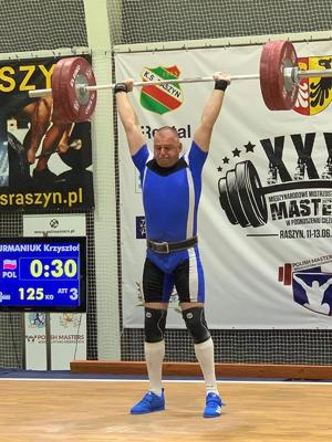 Aspirant sztabowy Krzysztof Furmaniuk trzyma sztangę w górze.