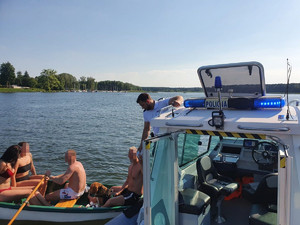 Policjanci kontrolują łódkę pływającą po Zalewie Koronowskim z 4 osobami i psem.