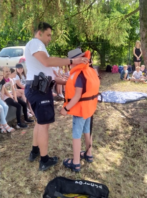 Policjant zakłada dziecku kamizelkę ratunkową.