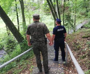 Policjant i leśnik idą po ażurowych schodach w lesie.