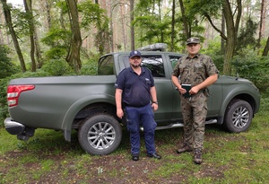 Policjant i leśnik stoją przed terenowym pojazdem służbowym leśników.