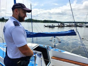 Policjant przygląda się przycumowanemu do nabrzeża jachtowi.