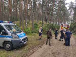 Policjanci i strażacy podczas kontroli obozowiska w terenie leśnym.