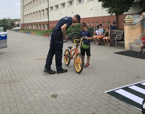 Policjant pokazuje uczniowi wyposażenie roweru.