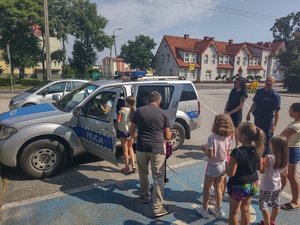 Dzieci oglądają policyjny radiowóz. Obok stoją policjanci.