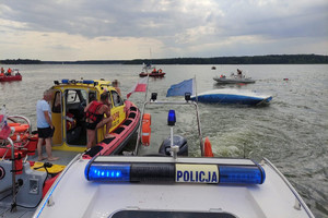dwie łodzie policyjna i WOPR-u odholowuje przewróconą łódź