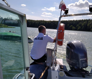 Policjant na policyjnej łodzi motorowej podczas wyciągania jachtu.