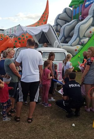 Policjant kuca wśród dzieci. W tle dmuchane zamki dla dzieci.