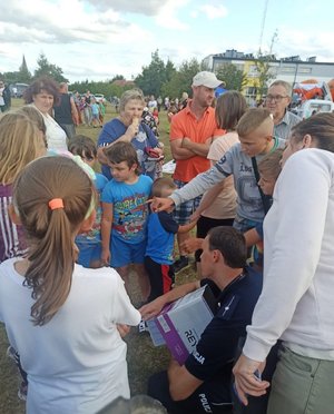 Policjant rozmawia z dziećmi kucając wśród nich.